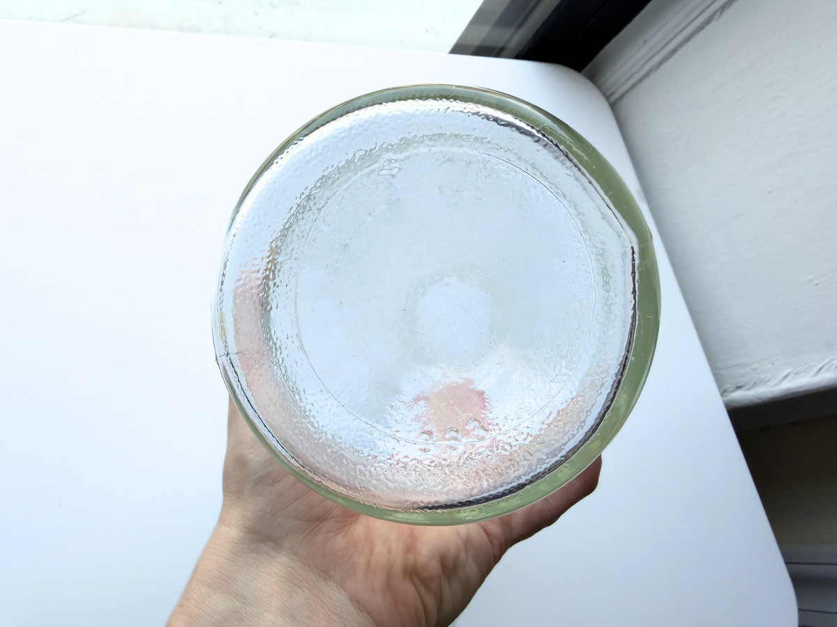 Hand cradling a vintage clear glass DAN-DEE jar, viewed from above into the opening