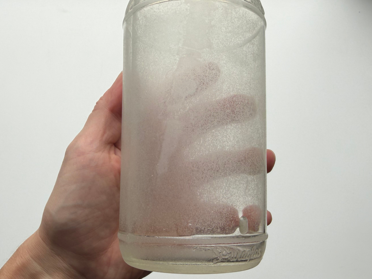 Hand holding a densely frosted sea glass Lavoris bottle to show its heavy sea-worn patina.