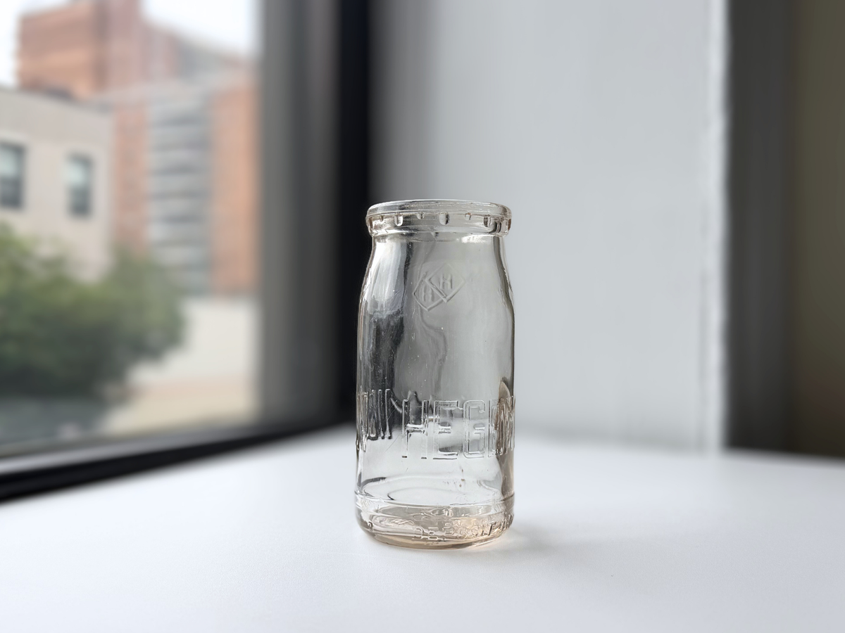Hegeman Farms milk bottle displayed on a windowsill with Brooklyn brownstones in the background.