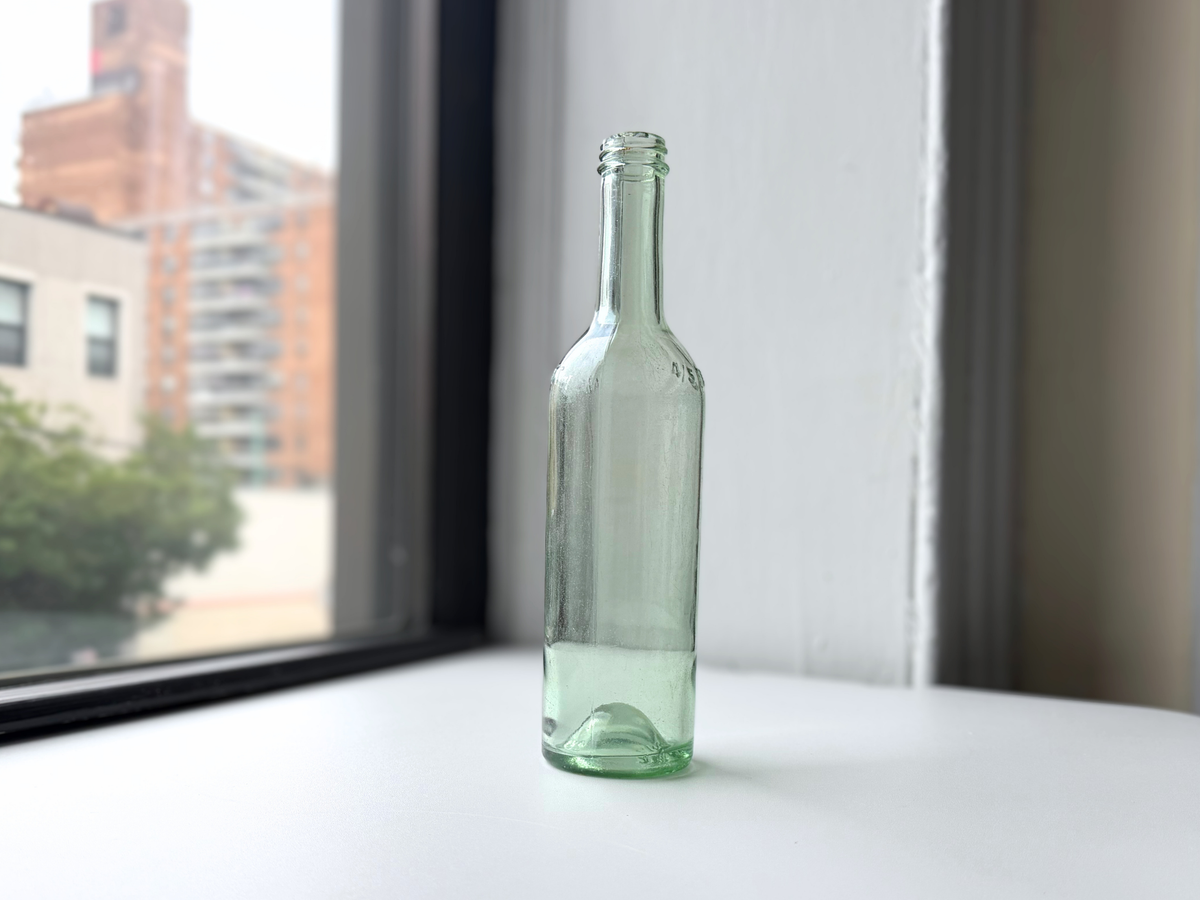 Pale green glass bottle on a windowsill at an angle, 1950s fortified wine packaging.