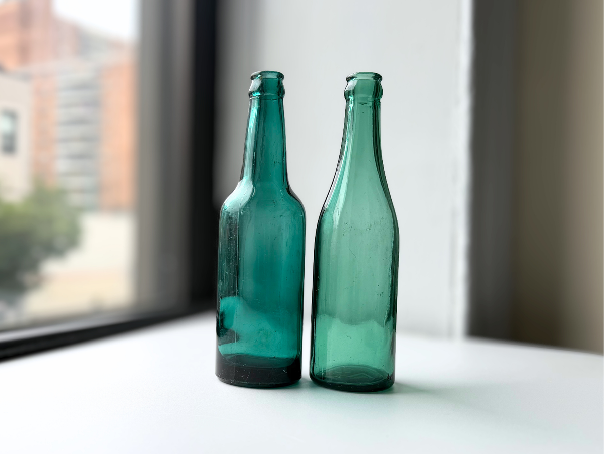 Teal and green glass beer bottles side by side on a sunlit windowsill.