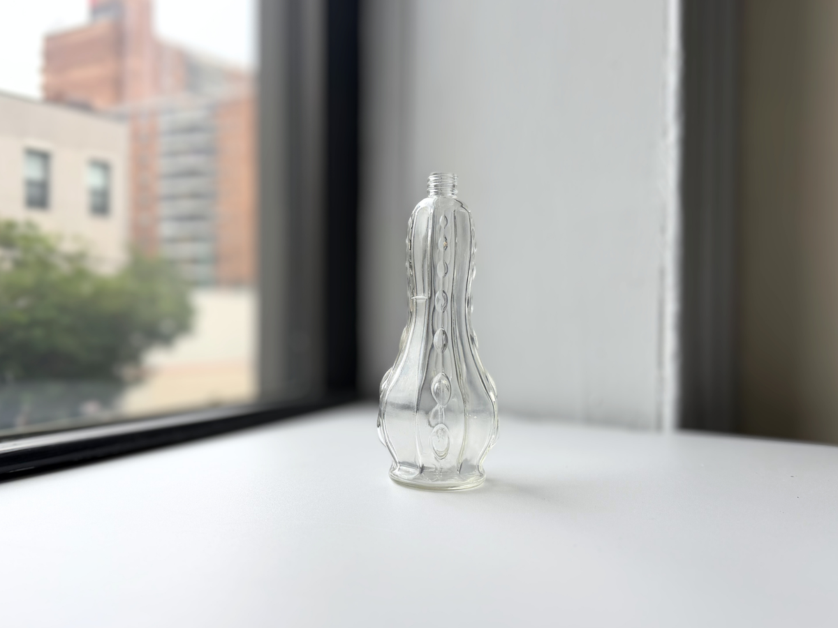 Textured teardrop glass bottle displayed on a windowsill with Brooklyn brownstones in the background.