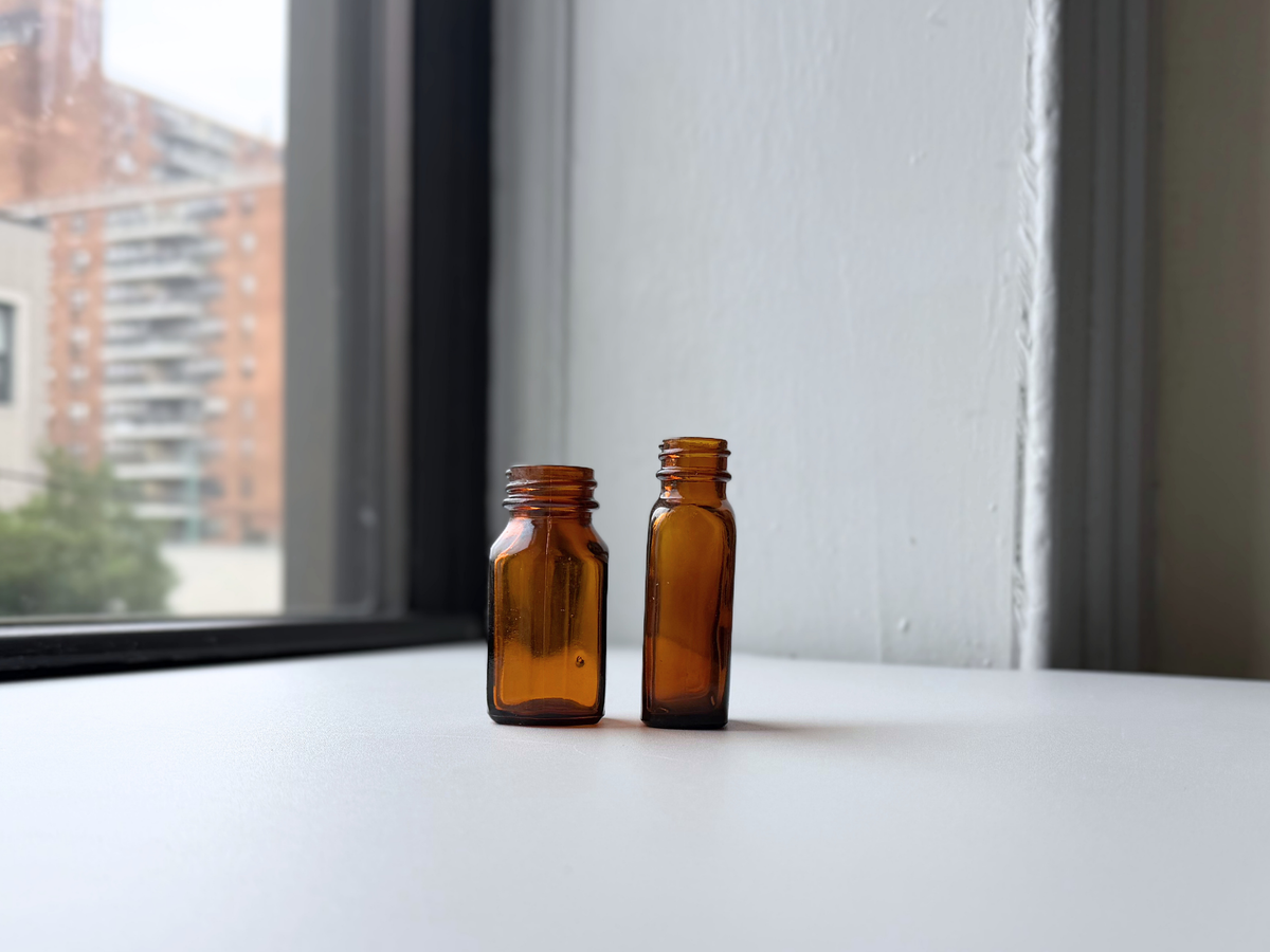 Set of two amber glass pharmacy bottles displayed on a windowsill with Brooklyn brownstones in the background.