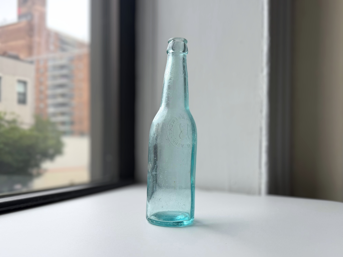 Fidelio Brewery aqua glass bottle displayed on a windowsill, side profile.