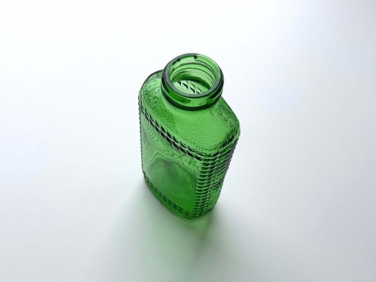 Vintage kelly green Airwick hobnail glass bottle photographed at an angle against a plain background