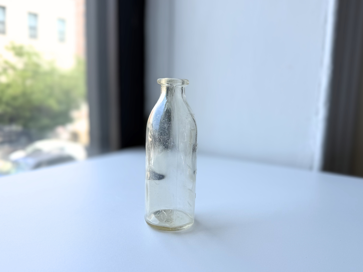 Brockway baby bottle close front view showing scratches and wear, clear glass