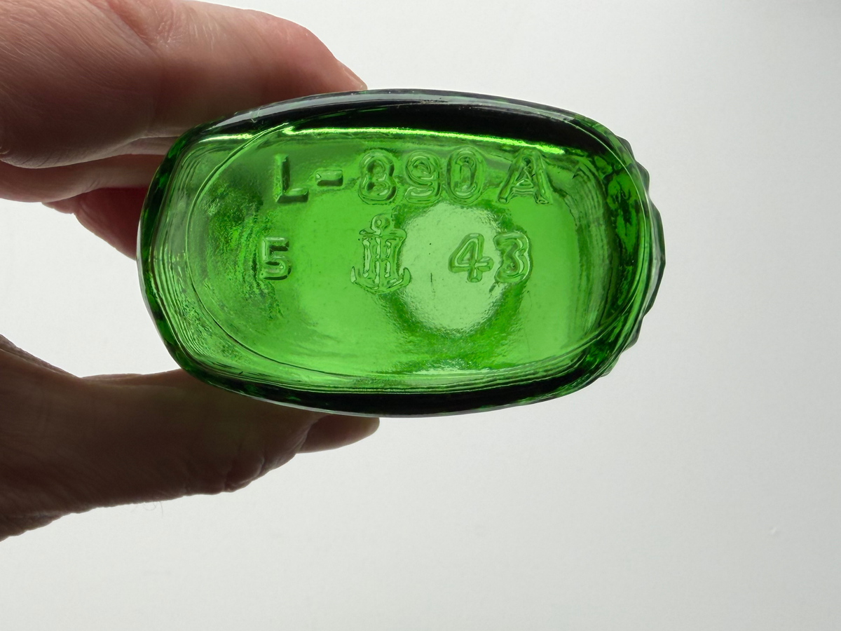 Hand holding a vintage kelly green Airwick bottle upside down showing the embossed L-890A mold number on the base