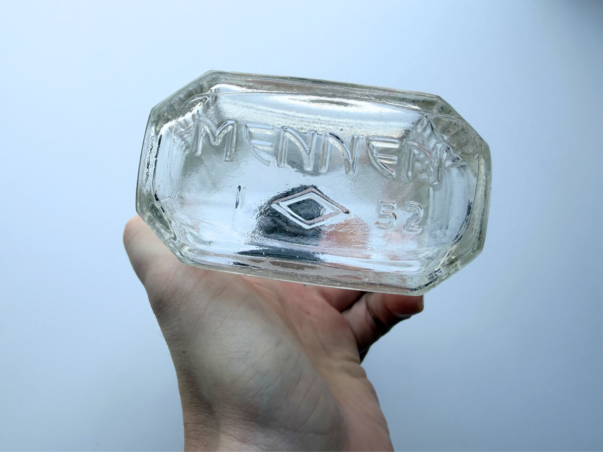 Hand holding Mennen bottle showing Art Deco pattern detail, clear glass
