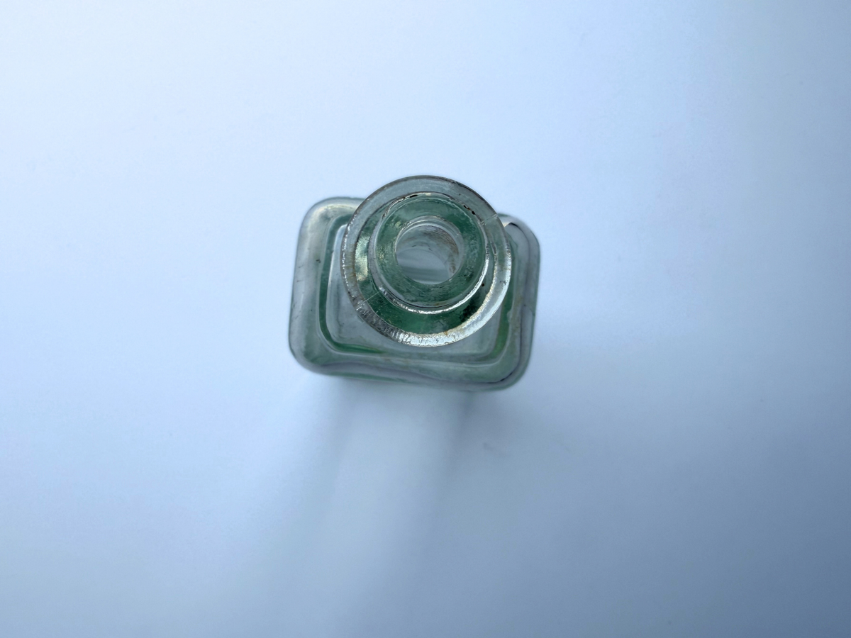 Top-down view into the open mouth of a vintage greenish-blue Polymol bottle