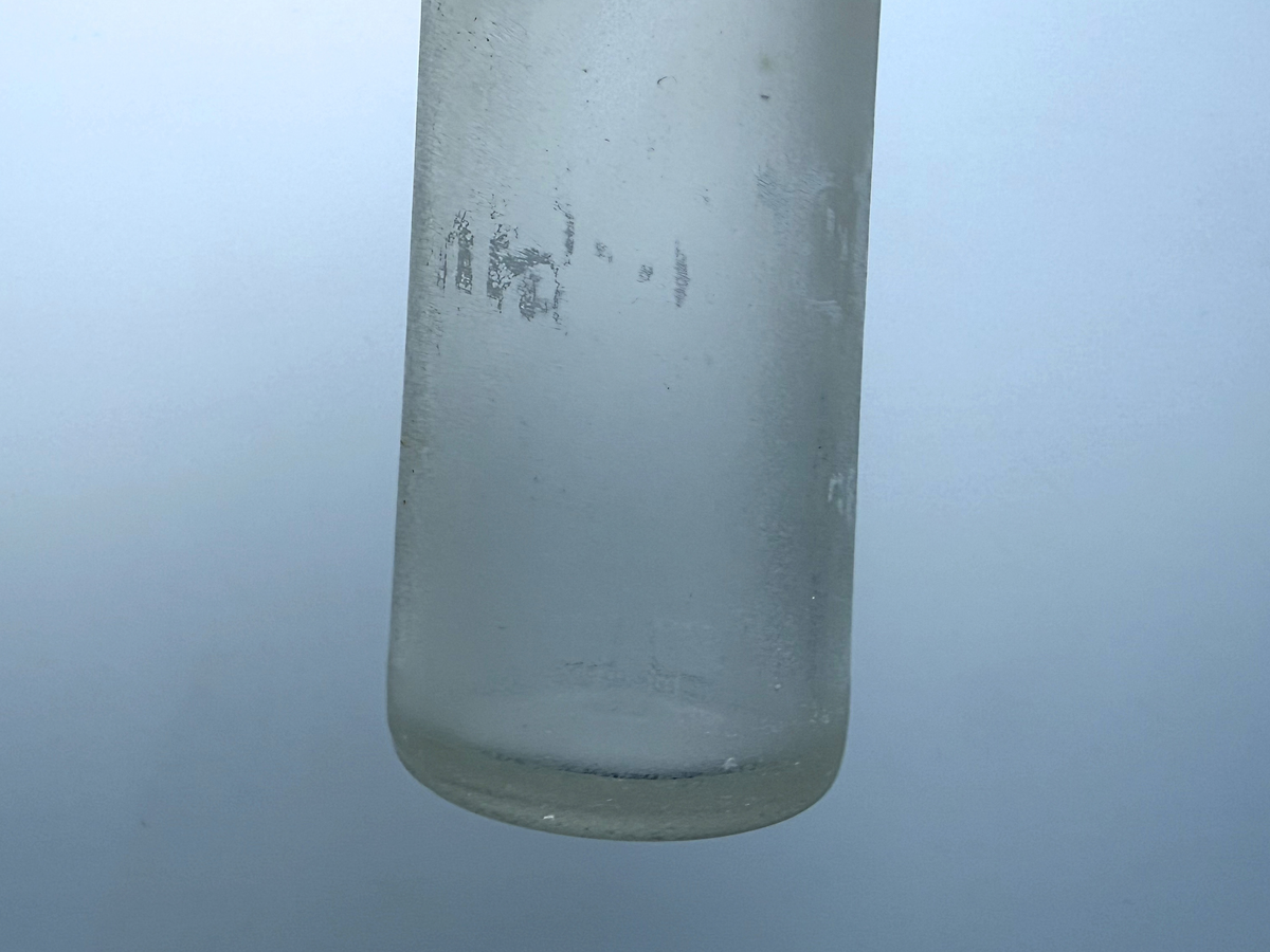 Frosted lower body of a sea-worn clear glass bottle with traces of faded lettering