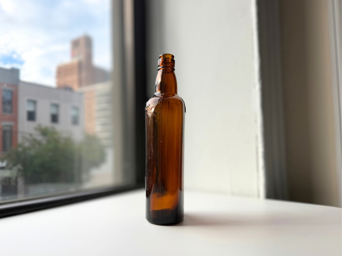 Side view of a vintage amber White Horse bottle on a windowsill, showing the mold seam running up the neck and body.