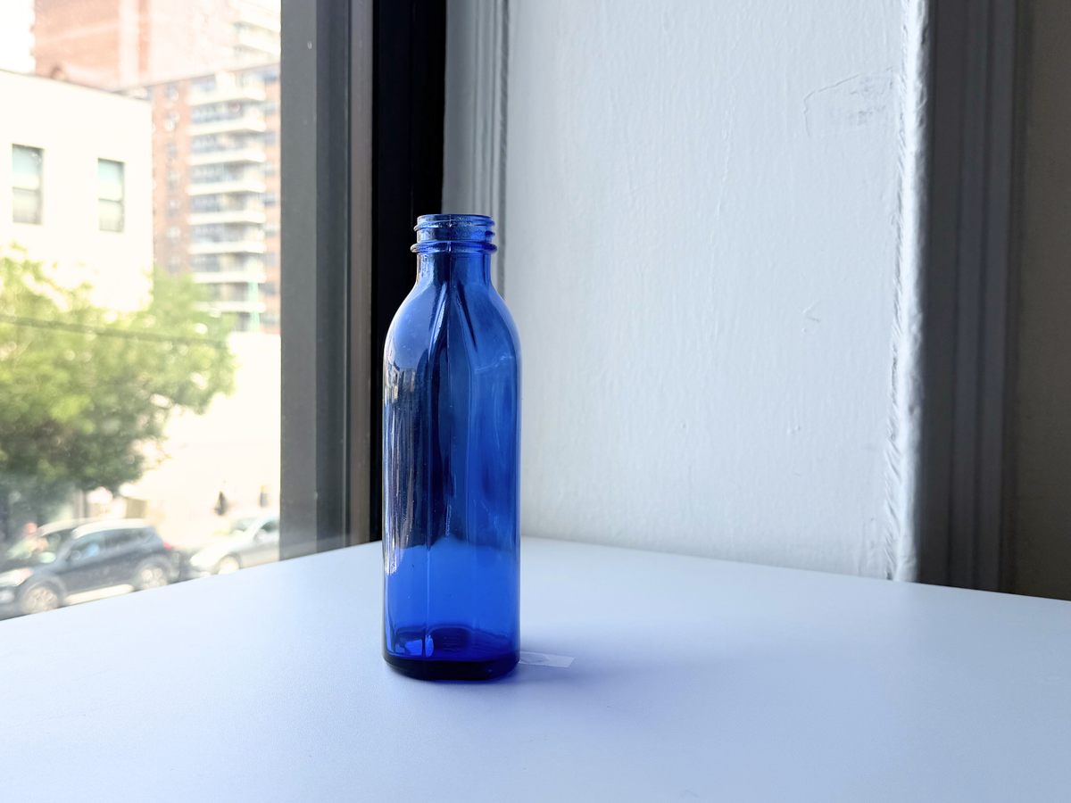 Tall Phillips cobalt blue bottle on windowsill with trees in background