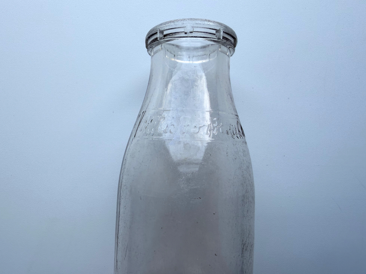 Close-up of the neck and shoulder of a vintage Milk for Health glass milk bottle, showing light haze