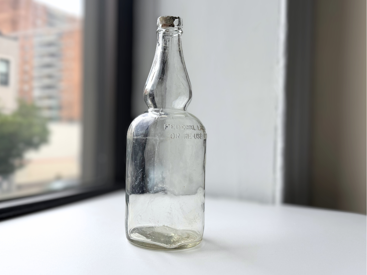 Antique James Martin & Co. whiskey bottle with visible cap remnant, photographed on a windowsill.