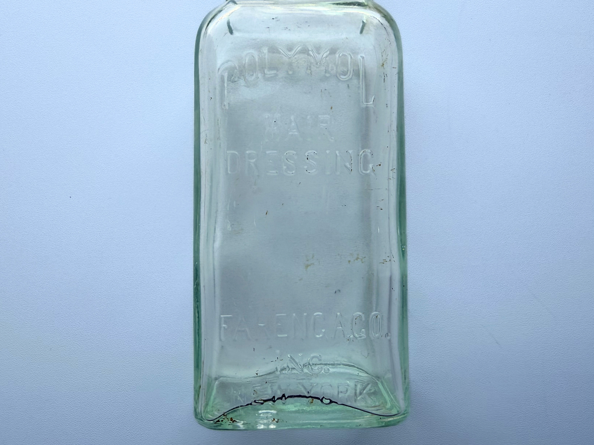 Close view of the embossed Polymol Hair Dressing Farenga Co Inc lettering on a pale aqua glass bottle