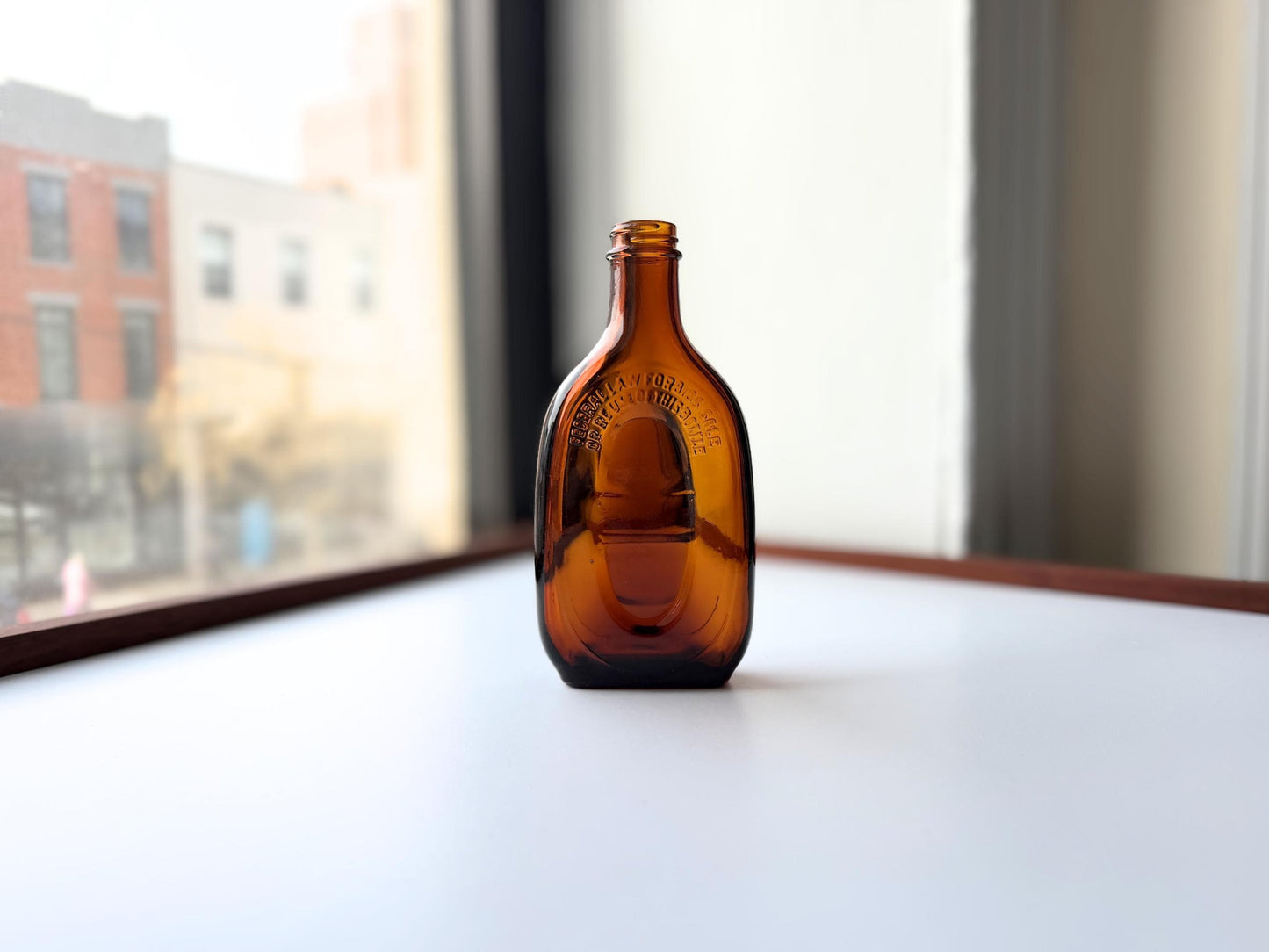 Vintage amber flat scotch bottle, 7 inches tall with ornate embossed front design, hand-recovered from NYC mid-century dumping grounds — authentic mid-century spirits bottle