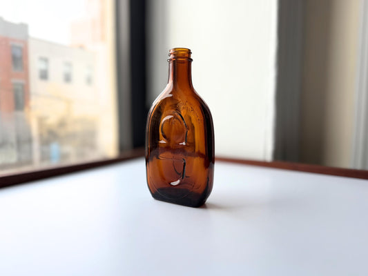 Vintage amber flat scotch bottle 7 inches tall with ornate embossed front design, hand-recovered from NYC mid-century dumping grounds – Brooklyn Sea Glass
