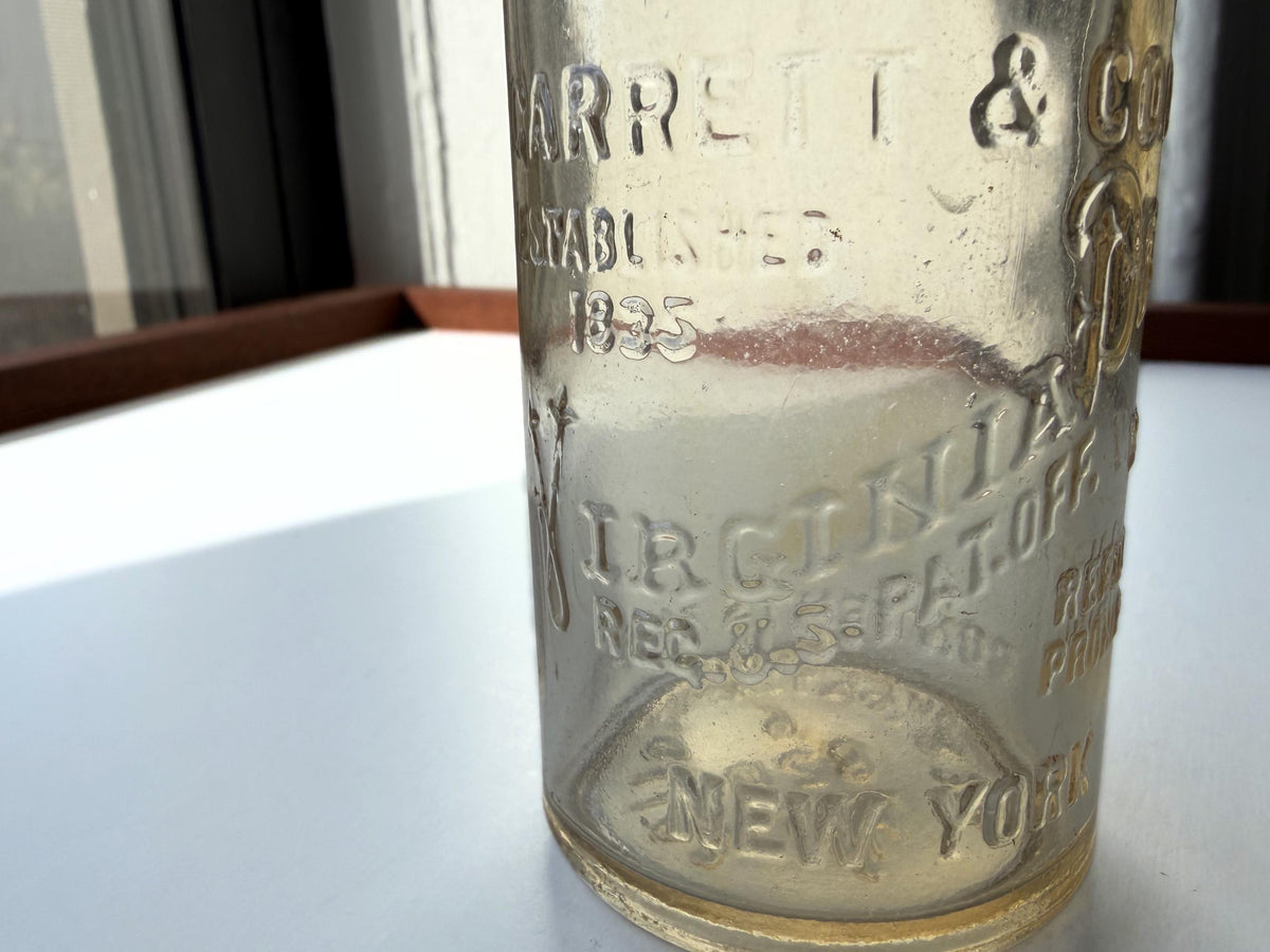 Close-up of VIRGINIA DARE front embossing and ESTABLISHED 1835 text on Garrett and Co clear glass bottle