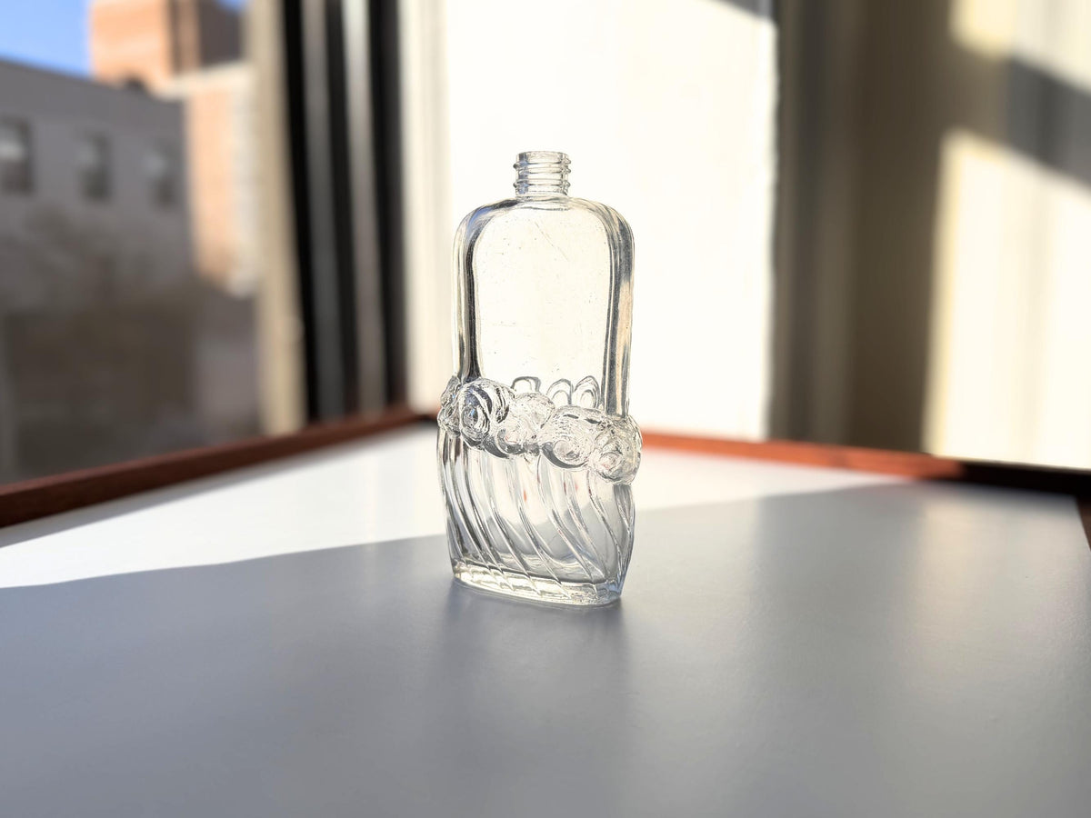 Wave-textured clear glass bottle backlit in window showing light shimmer effect through textured surface