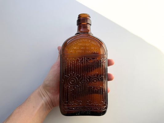 Close-up of HIRAM WALKER embossing on amber glass flask body, Canadian distillery branding clearly legible