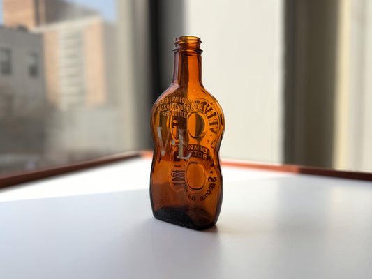 Vintage Velvet Edge amber dimple bottle 7 inches tall dated 1952 with figure-8 silhouette and Federal Law embossing - hand-recovered from NYC mid-century dumping grounds