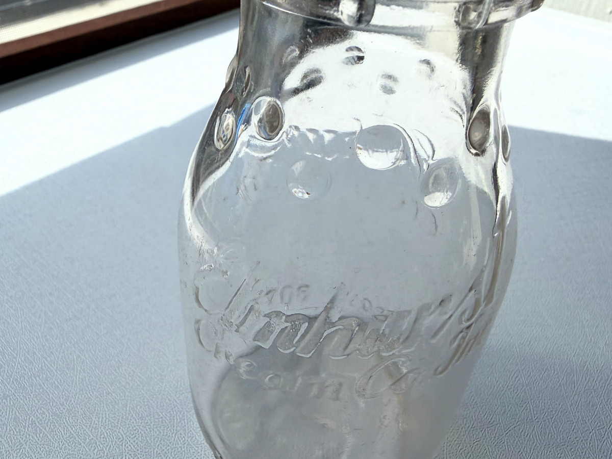 Elmhurst Cream Co. milk bottle back angle view showing ELMHURST CREAM CO INC reverse embossing on clear glass