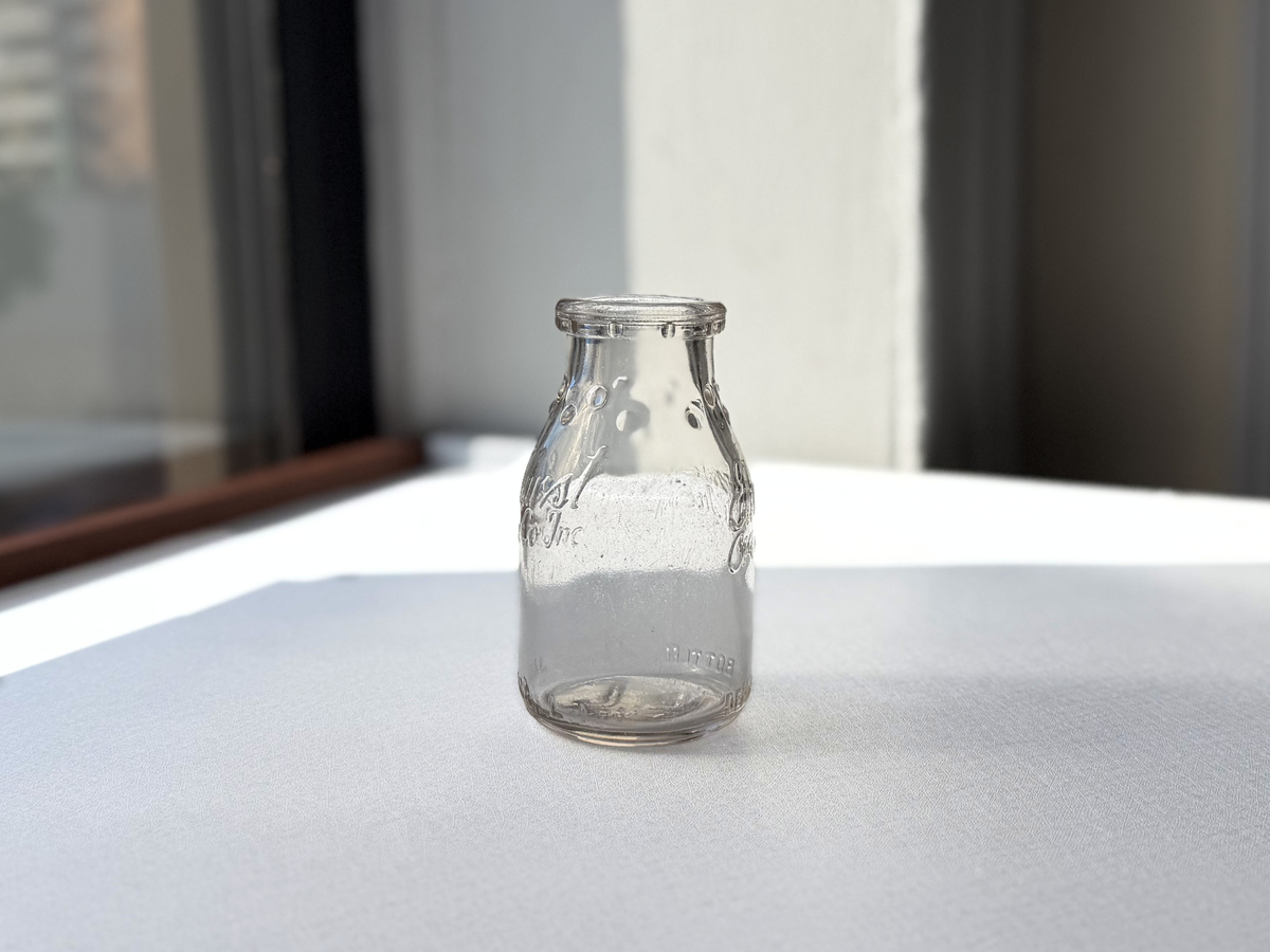 Elmhurst Cream Co. bottle front angle view showing clear glass form and dual-face embossed branding, NYC recovery