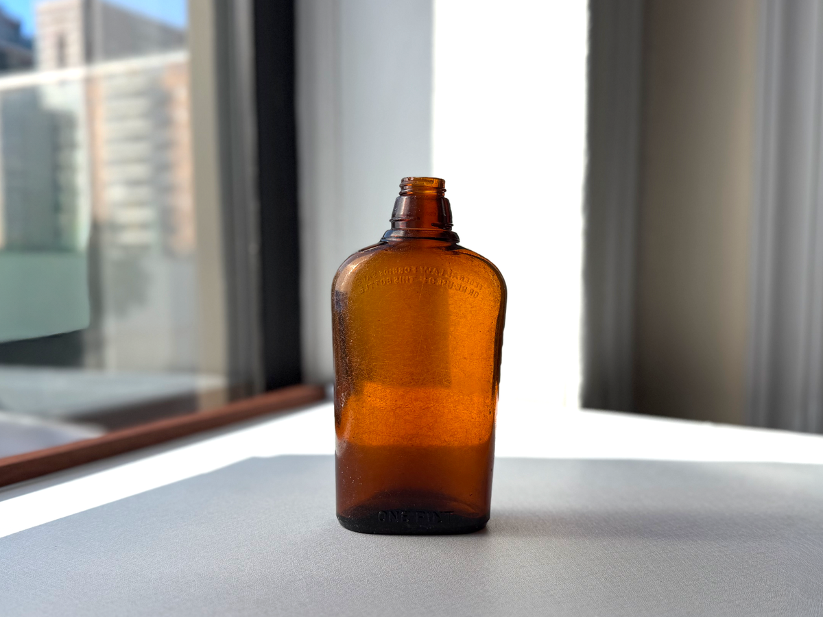 Federal Law wide-shoulder amber flask front view in window light showing seaworn frosted surface texture