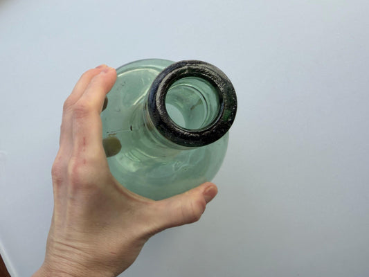Vintage sage green hand-blown bottle angled view, natural glass variation and pontil base, cottagecore display