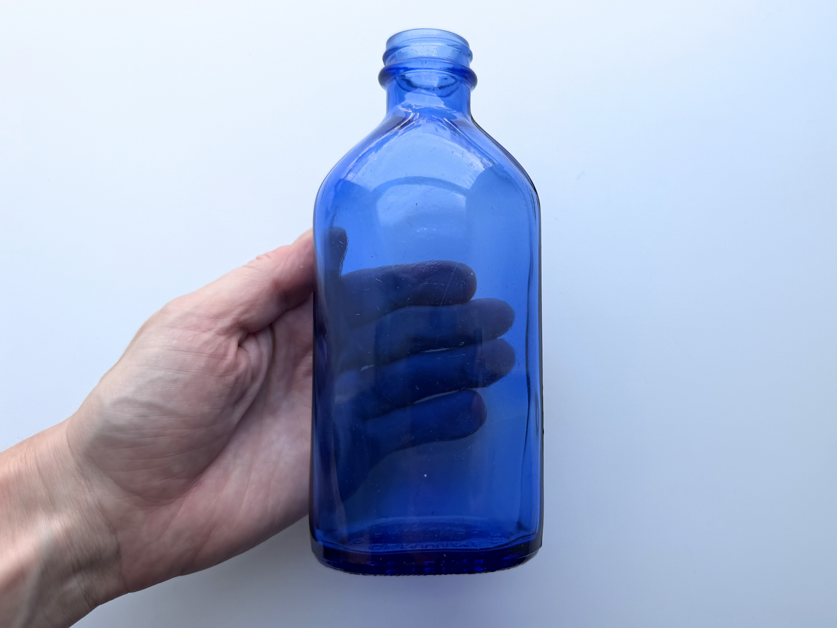 Hand holding medium Phillips cobalt blue bottle for scale