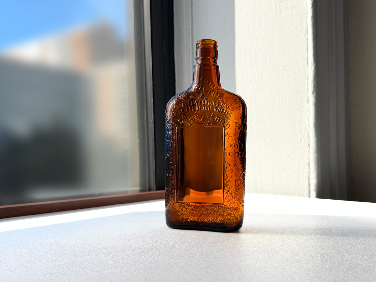 Lord Calvert Men of Distinction amber flask styled on bar cart surface, flat flask form and warm amber glass