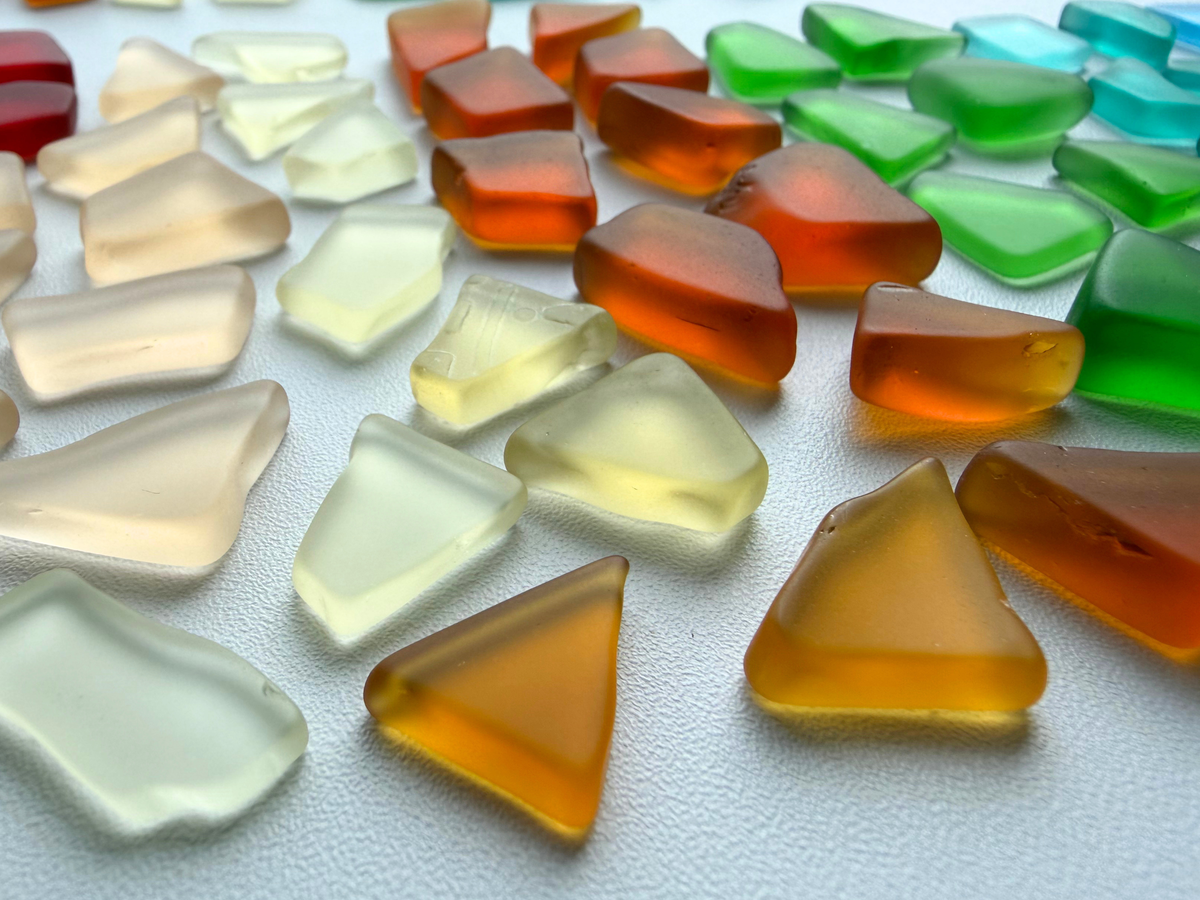 Close-up pile of small assorted color tumbled sea glass with smooth frosted texture, showing the natural mix of blues, greens, and warm tones used in jewelry and mosaic art.