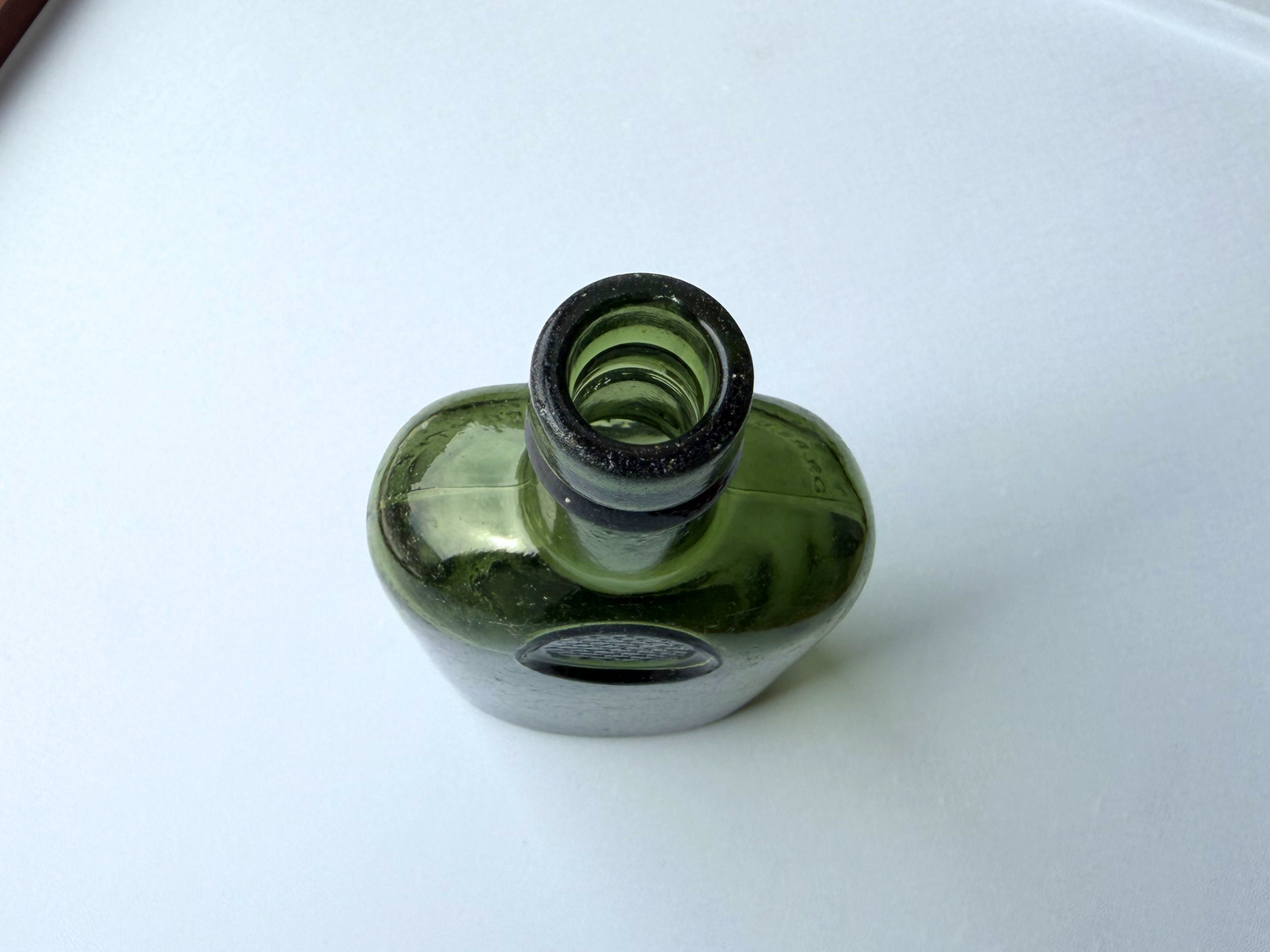 Top-down view of a vintage green glass Sanderson bottle, showing the narrow neck opening and rounded shoulder from above.