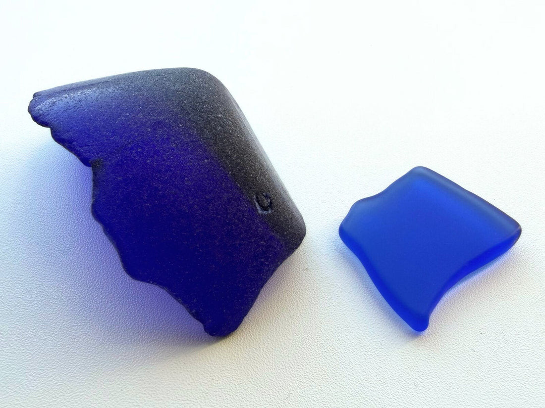 A genuine cobalt blue sea glass piece with heavy pitting and dark patina beside a smooth, evenly frosted machine-tumbled cobalt piece.