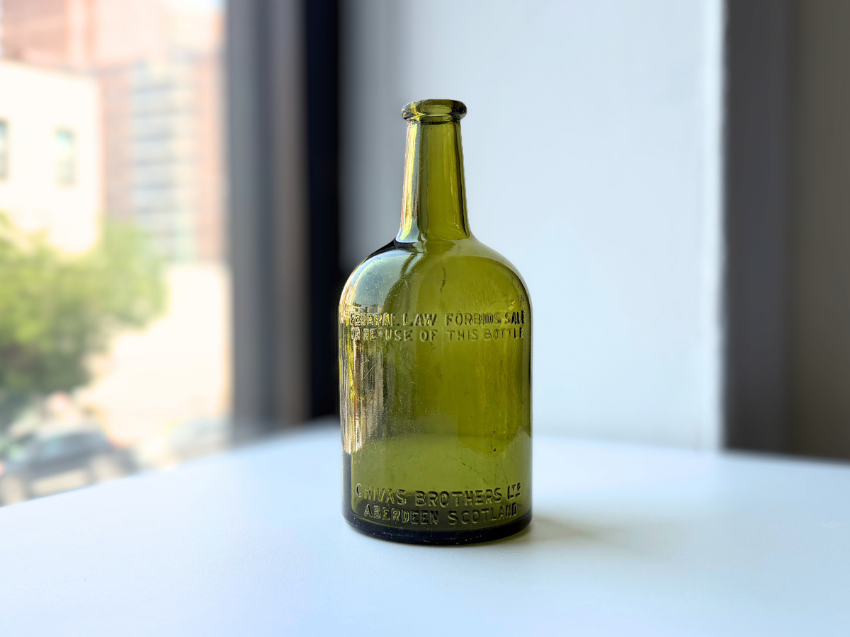 Vintage light olive green Chivas Brothers Aberdeen Scotland bottle with embossed lettering on a sunny windowsill