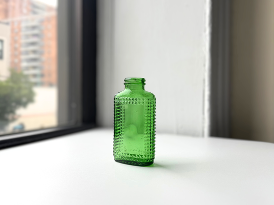 Vintage kelly green Airwick hobnail glass bottle sitting on a windowsill, front view