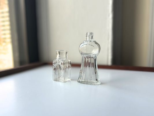 Vintage clear glass Helena Rubinstein and Kerkoff perfume bottle set side by side on a sunny windowsill