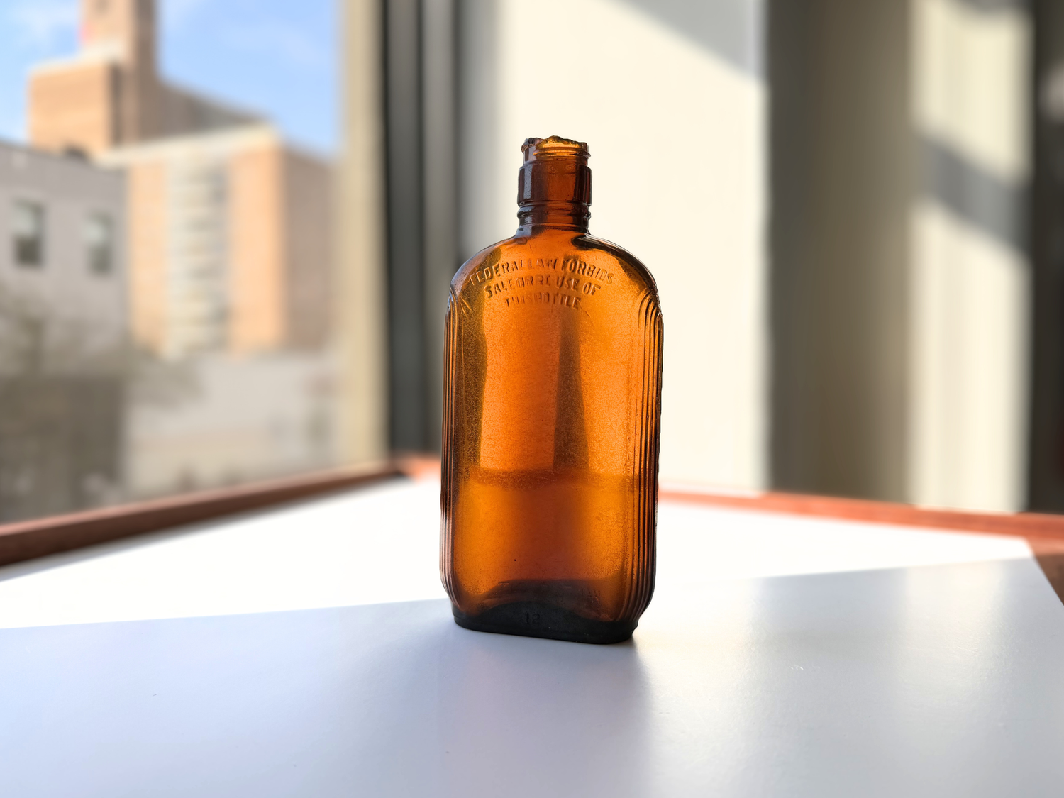 Sea-worn amber glass Art Deco flask, front view on a sunlit windowsill