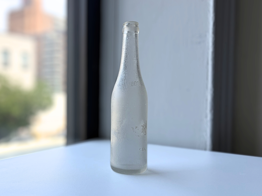 Sea-worn frosted clear glass Hollywood soda bottle standing on a sunny windowsill