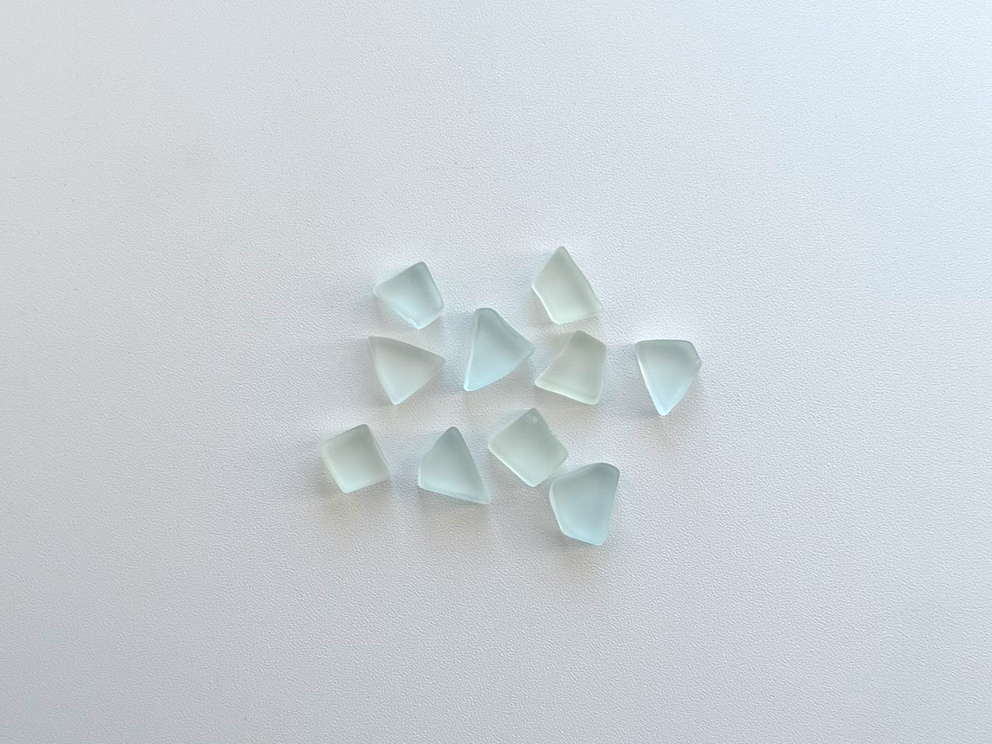 Small pile of pale seafoam and sky blue tumbled sea glass pieces, flat on two sides