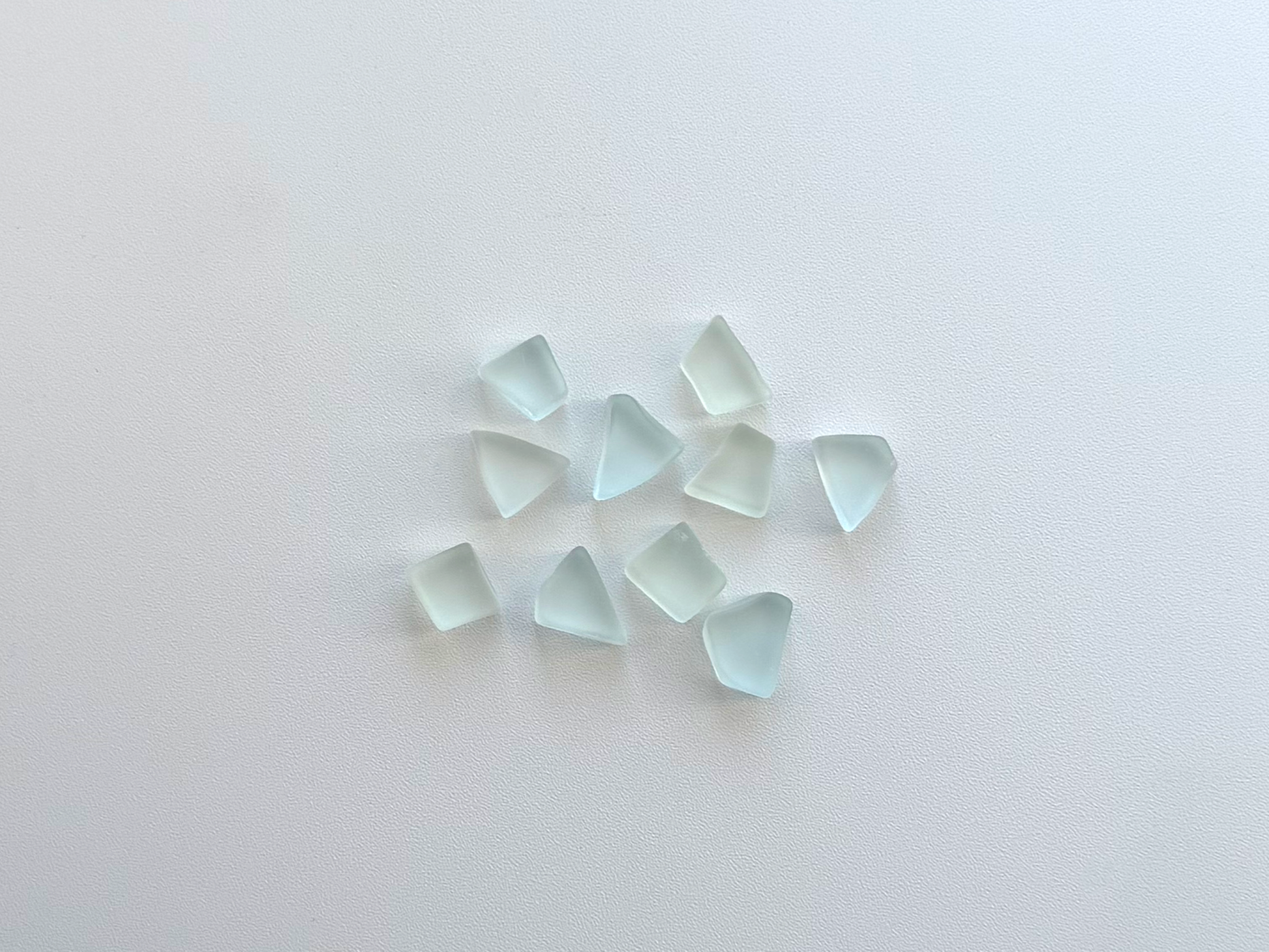 Small pile of pale seafoam and sky blue tumbled sea glass pieces, flat on two sides