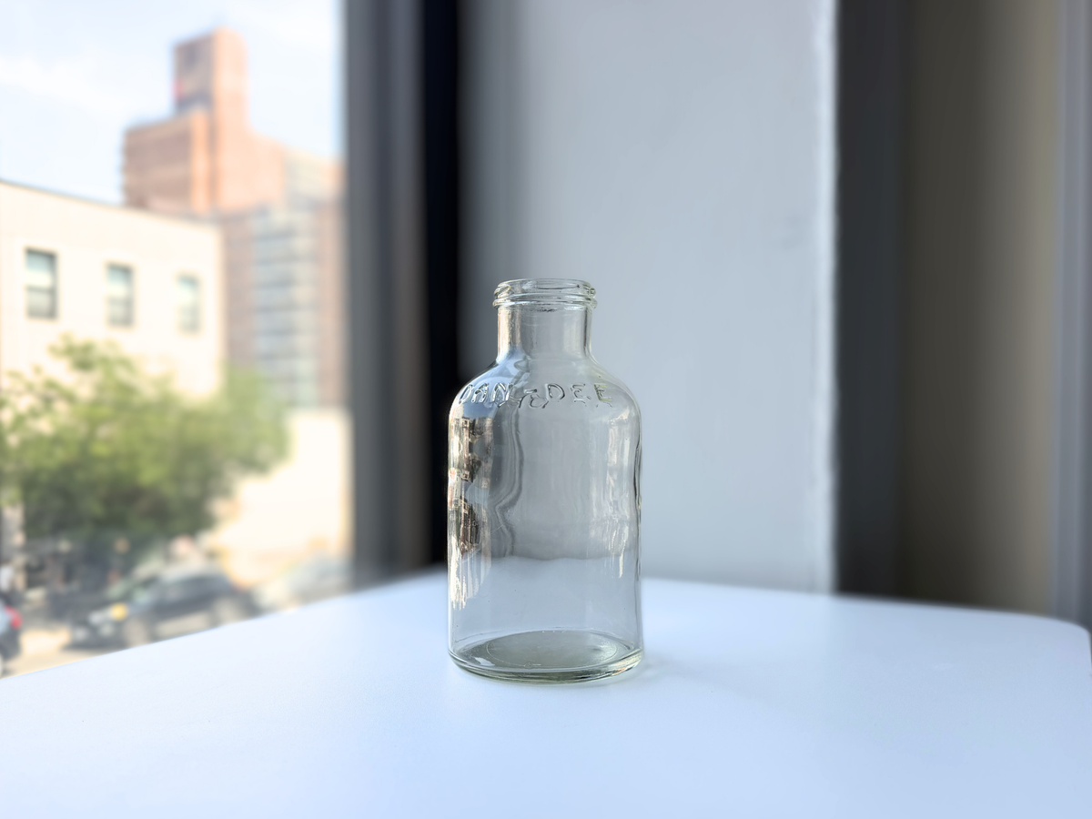 Vintage clear glass DAN-DEE jar photographed on a windowsill with city buildings in the background