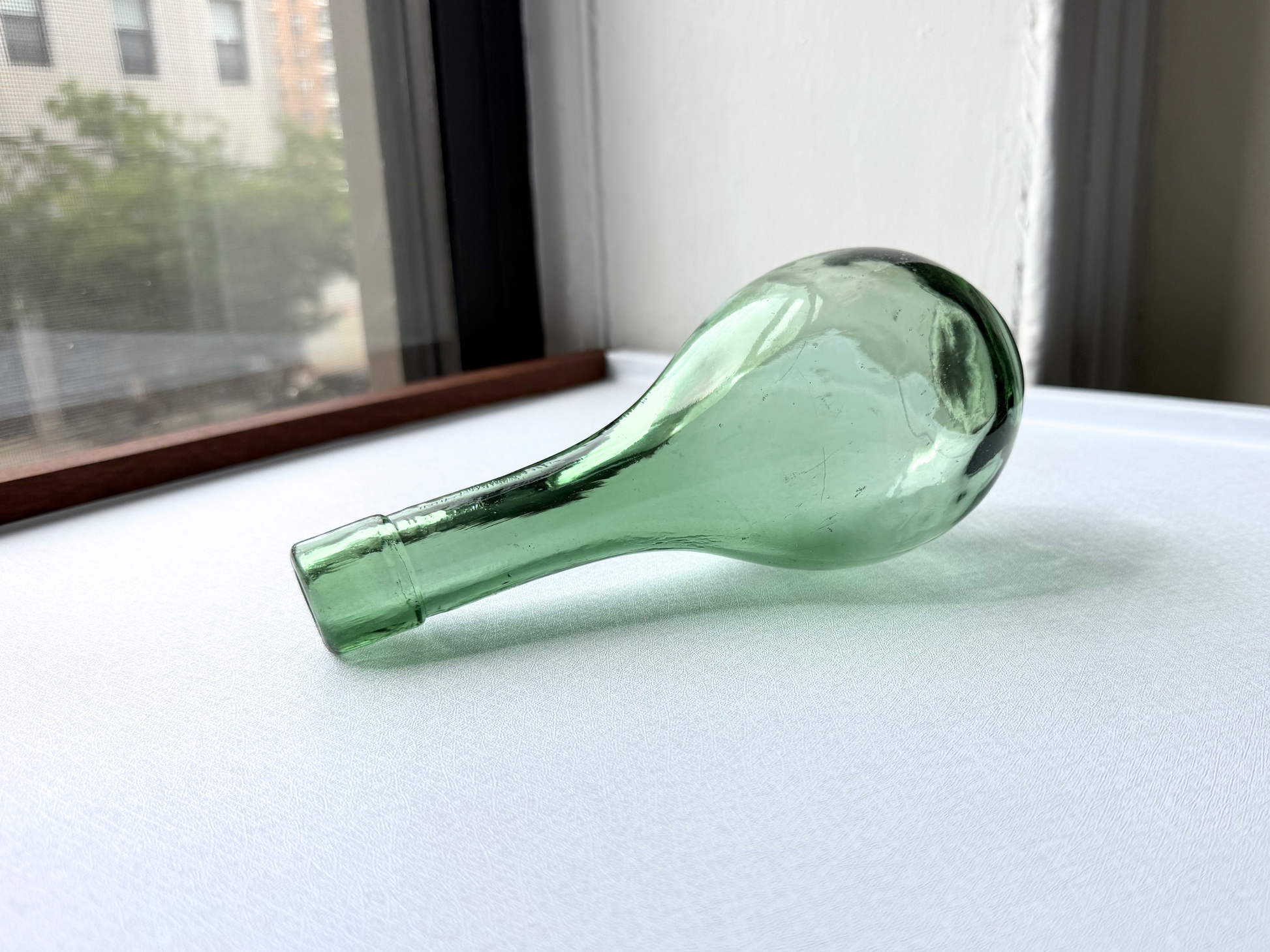 Vintage green glass teardrop bottle shown in side profile, showcasing its curved silhouette
