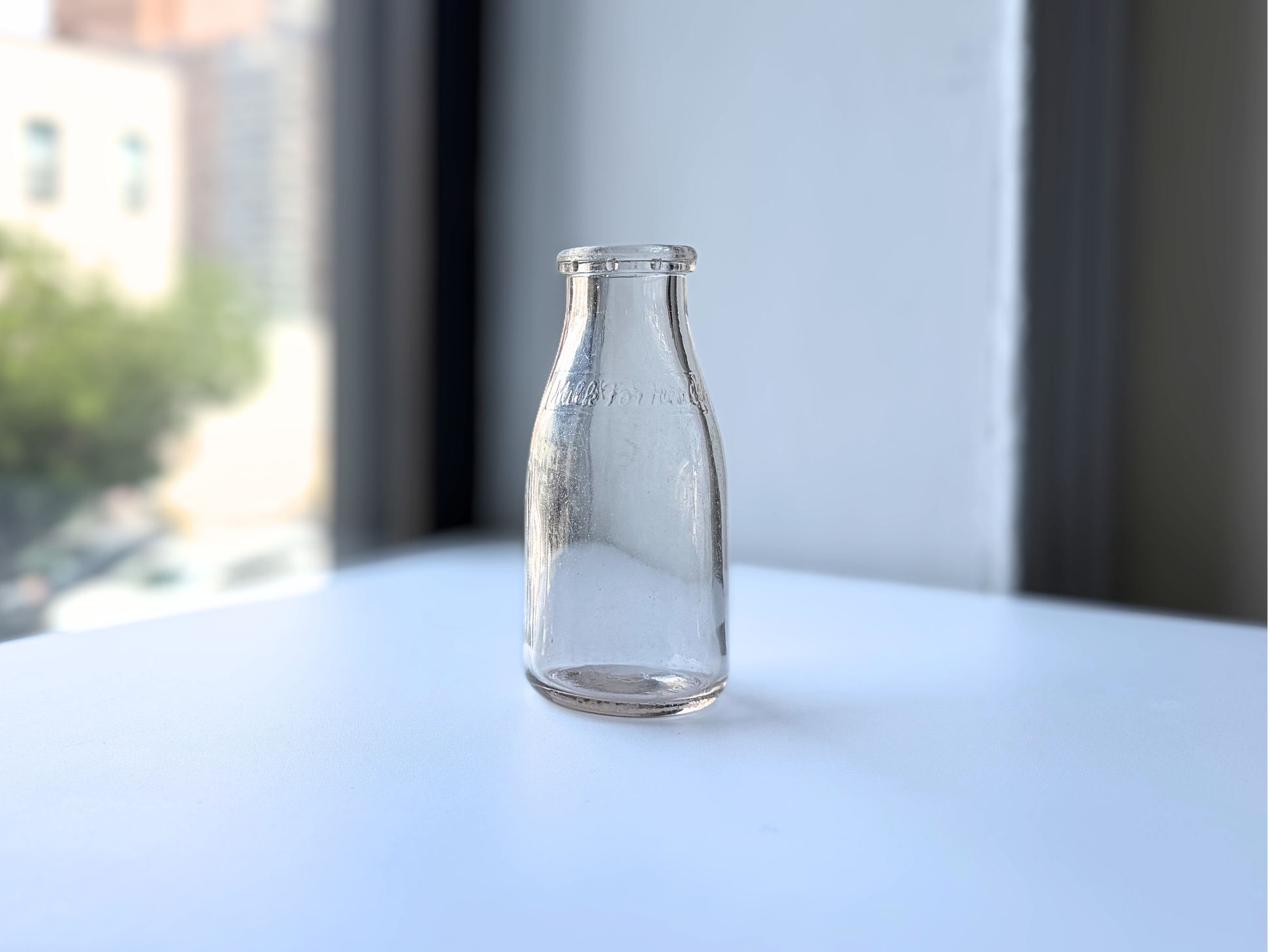 Vintage clear glass Milk for Health bottle on a windowsill with city buildings in the background