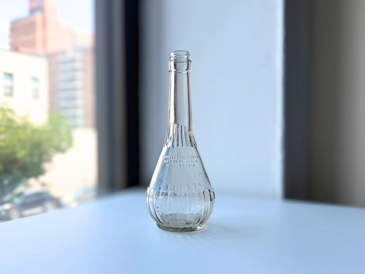 Vintage ribbed clear glass genie bottle standing on a sunny windowsill with city buildings behind it
