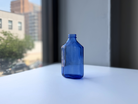 Vintage periwinkle blue Squibb medicine bottle standing on a windowsill, full front view