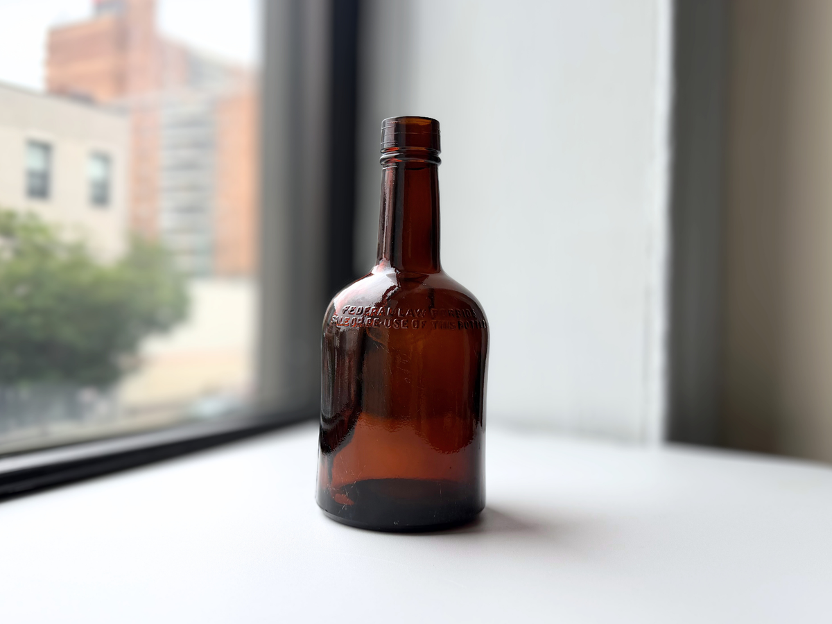 Dark amber glass whiskey bottle from 1953 shown at an angle on a windowsill.