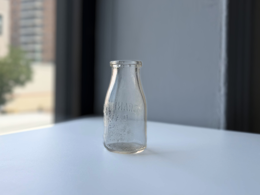 Clear glass Grandview Dairy bottle from Brooklyn NY, side view in natural window light