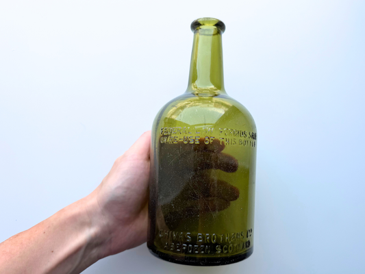 Hand holding a vintage light olive green Chivas Brothers glass bottle to show its scale
