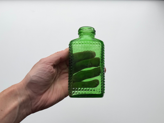 Hand holding a vintage kelly green Airwick hobnail glass bottle to show scale